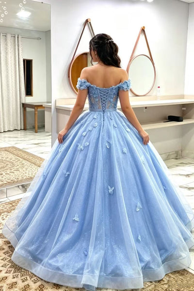 A woman wearing a voluminous light blue ball gown with off-the-shoulder straps, a lace-up corset-style back, and embroidered butterfly details, photographed in a boutique interior.